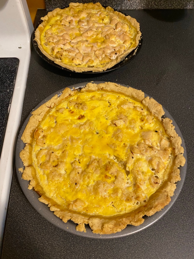 Yellow-coloured pie in its pan, sitting on a dark grey counter. A second pie is in the background.